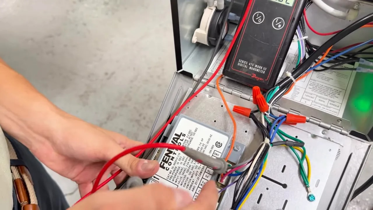 Multimeter probes testing wiring at the radiant heater circuit board beside a glowing green indicator light