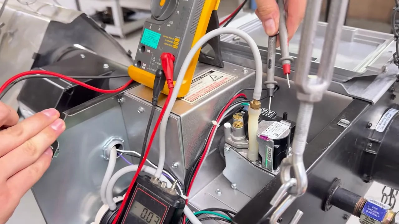 Multimeter probes positioned at the gas valve terminals on a radiant heater burner